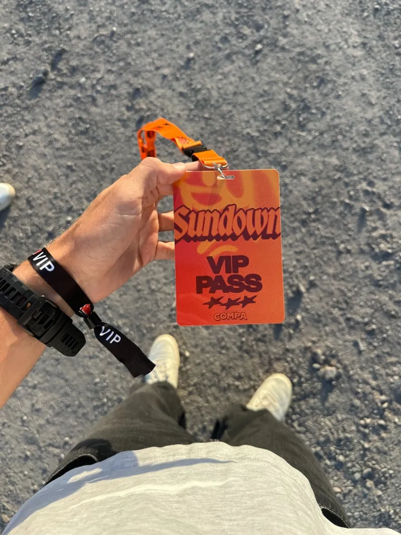 A hand holding an orange Sundown VIP pass on a lanyard, with a VIP wristband